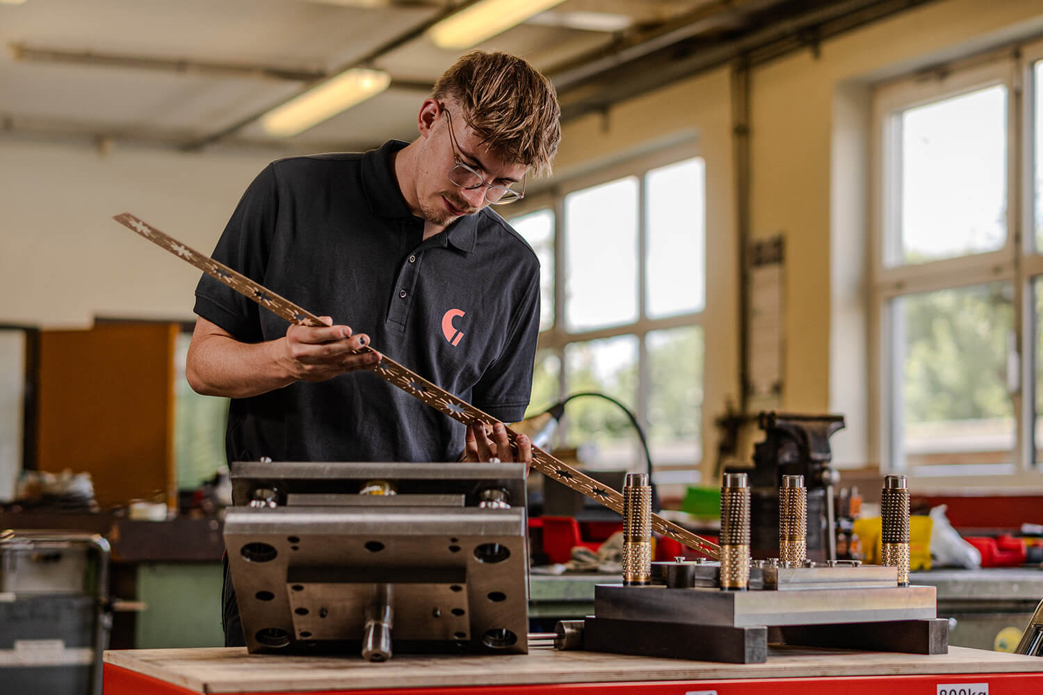 Ein Mitarbeiter mit Brille im Grashorn-Polohemd prüft ein langes, filigranes Stanzwerkzeug in der Werkstatt.