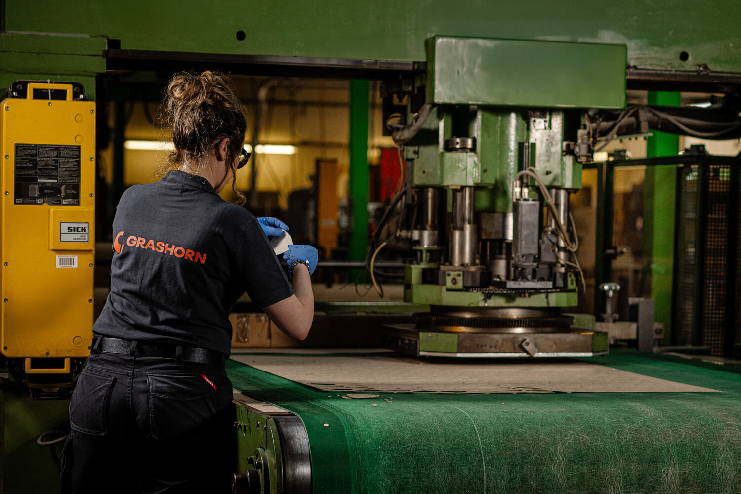 Mitarbeiterin bedienen eine große, grüne Stanzmaschine in einer Produktionshalle.