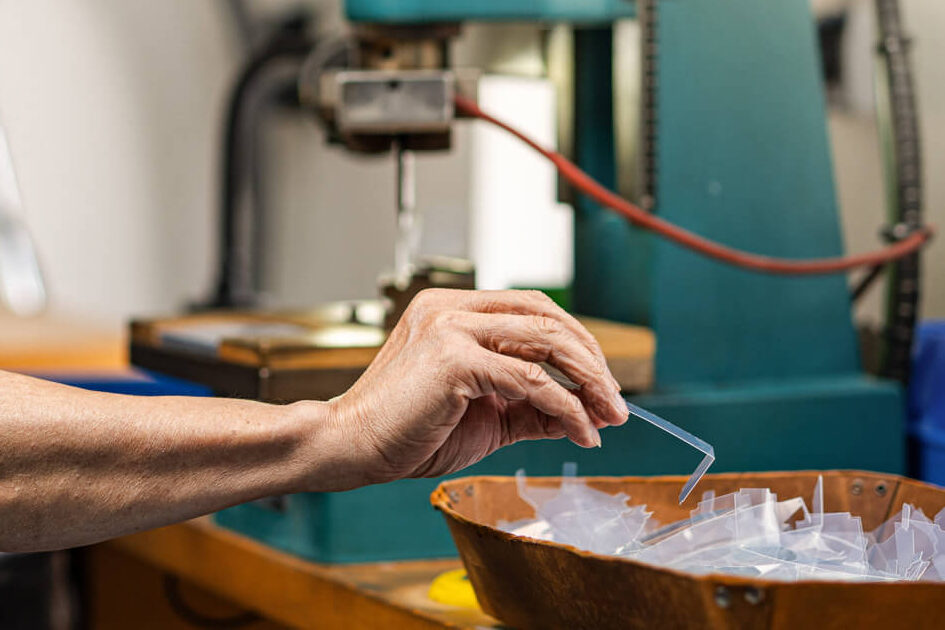 Ein Mitarbeiter bei Grashorn prüft kleine, transparente Kunststoff-Stanzteil an einer Maschine in der Fertigung.