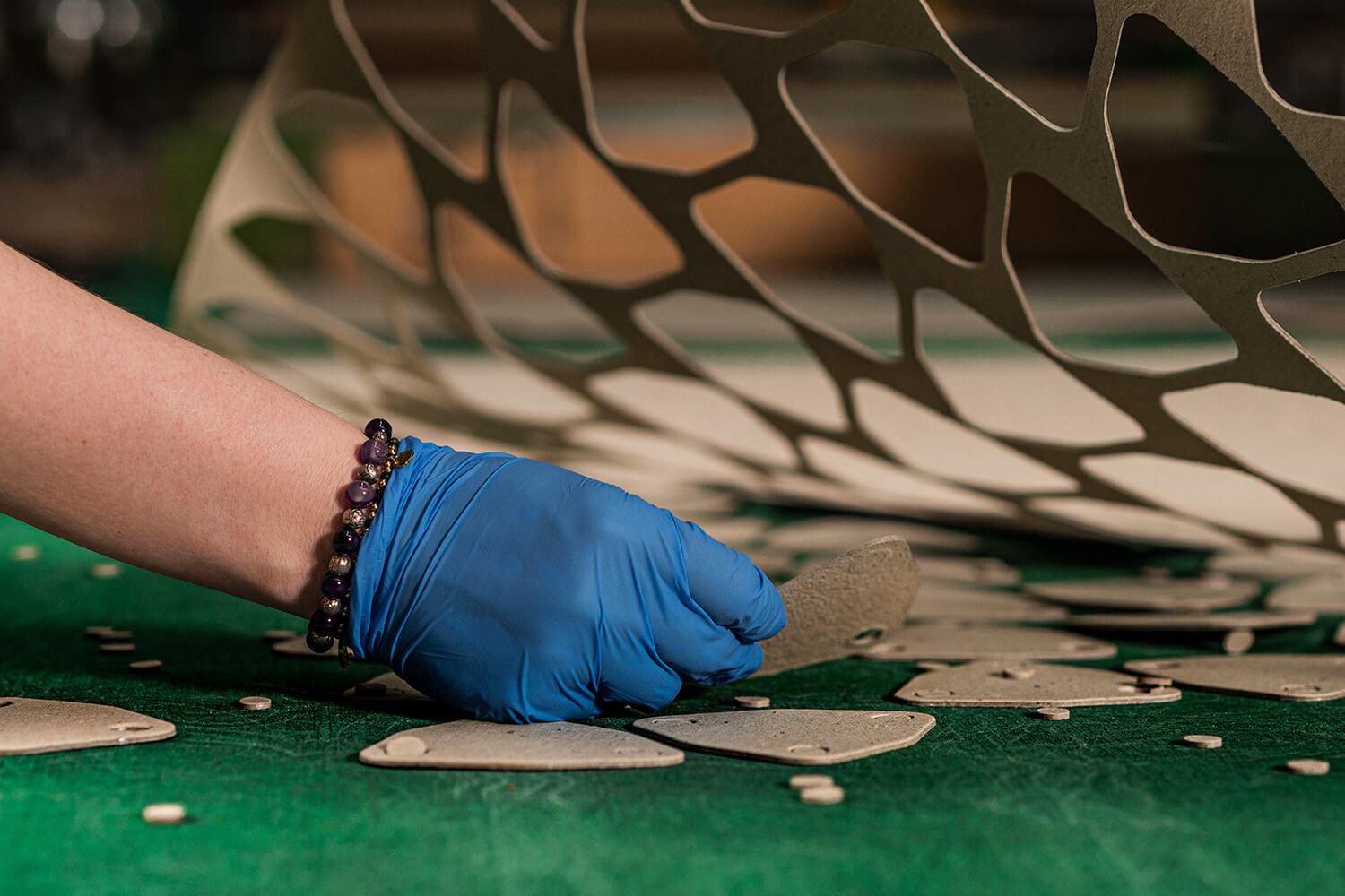 Eine Hand mit blauem Handschuh entnimmt ein frisch gestanztes Teil von einer grünen Fertigungsmatte.