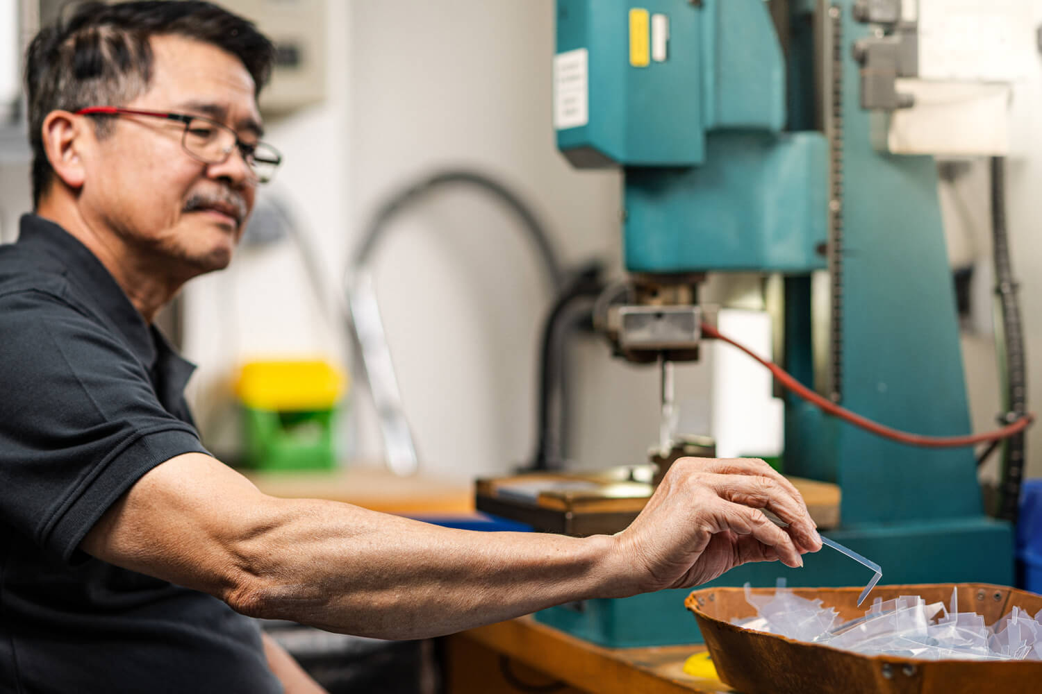 Ein Mitarbeiter bei Grashorn prüft kleine, transparente Kunststoff-Stanzteil an einer Maschine in der Fertigung.