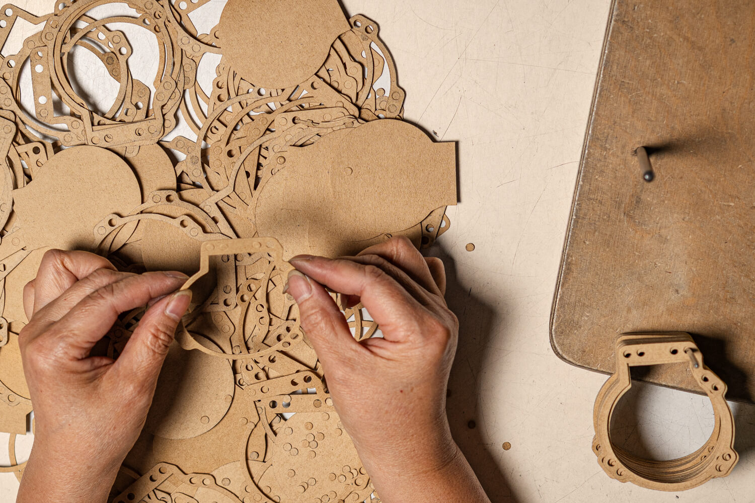 Hände sortieren eine große Menge an präzise gestanzten Teilen aus einem braunen Werkstoff auf einem Arbeitstisch.