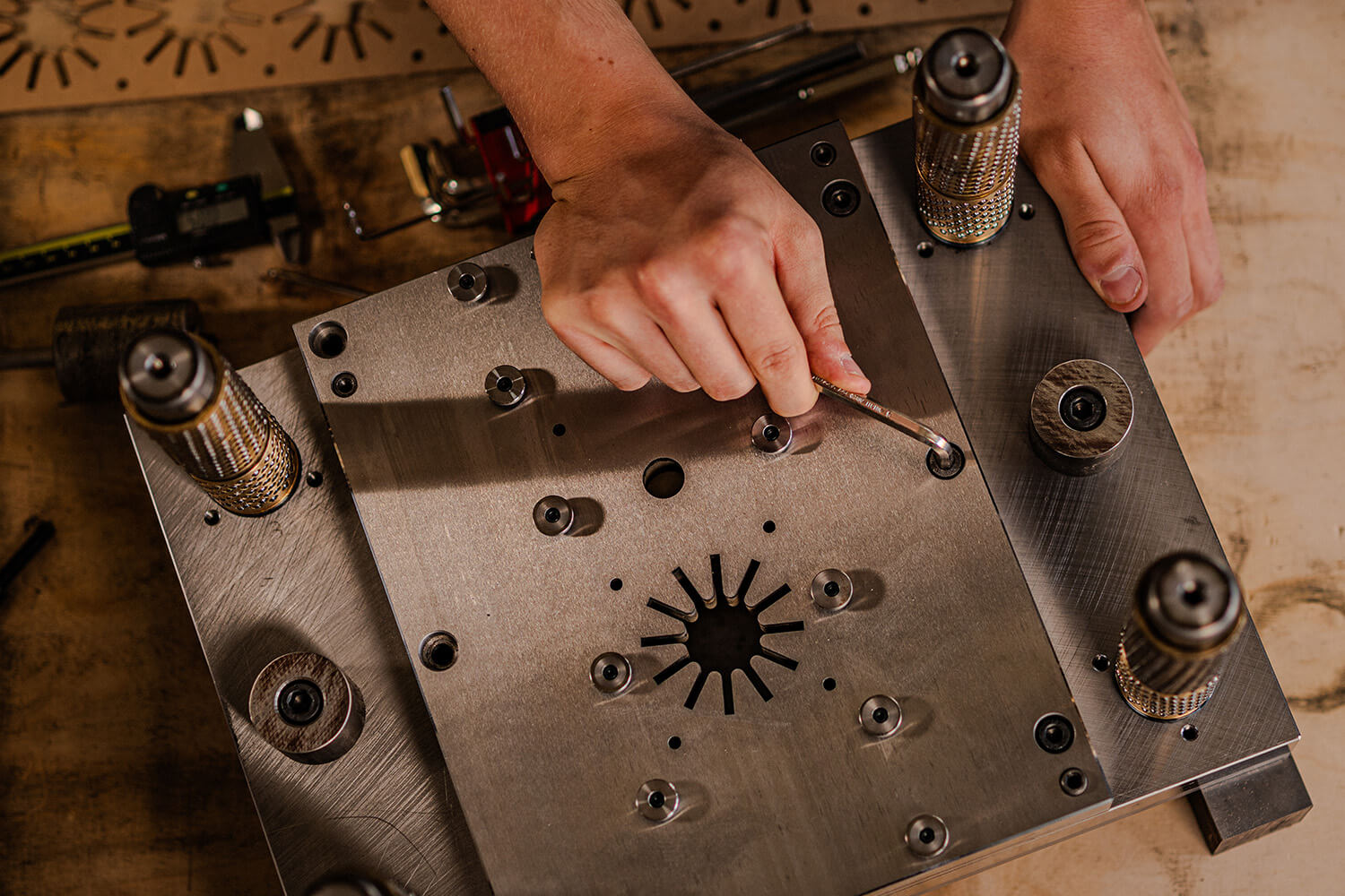 Nahaufnahme von Händen, die mit einem Werkzeug präzise an einem komplexen Stanzwerkzeug aus Metall arbeiten.