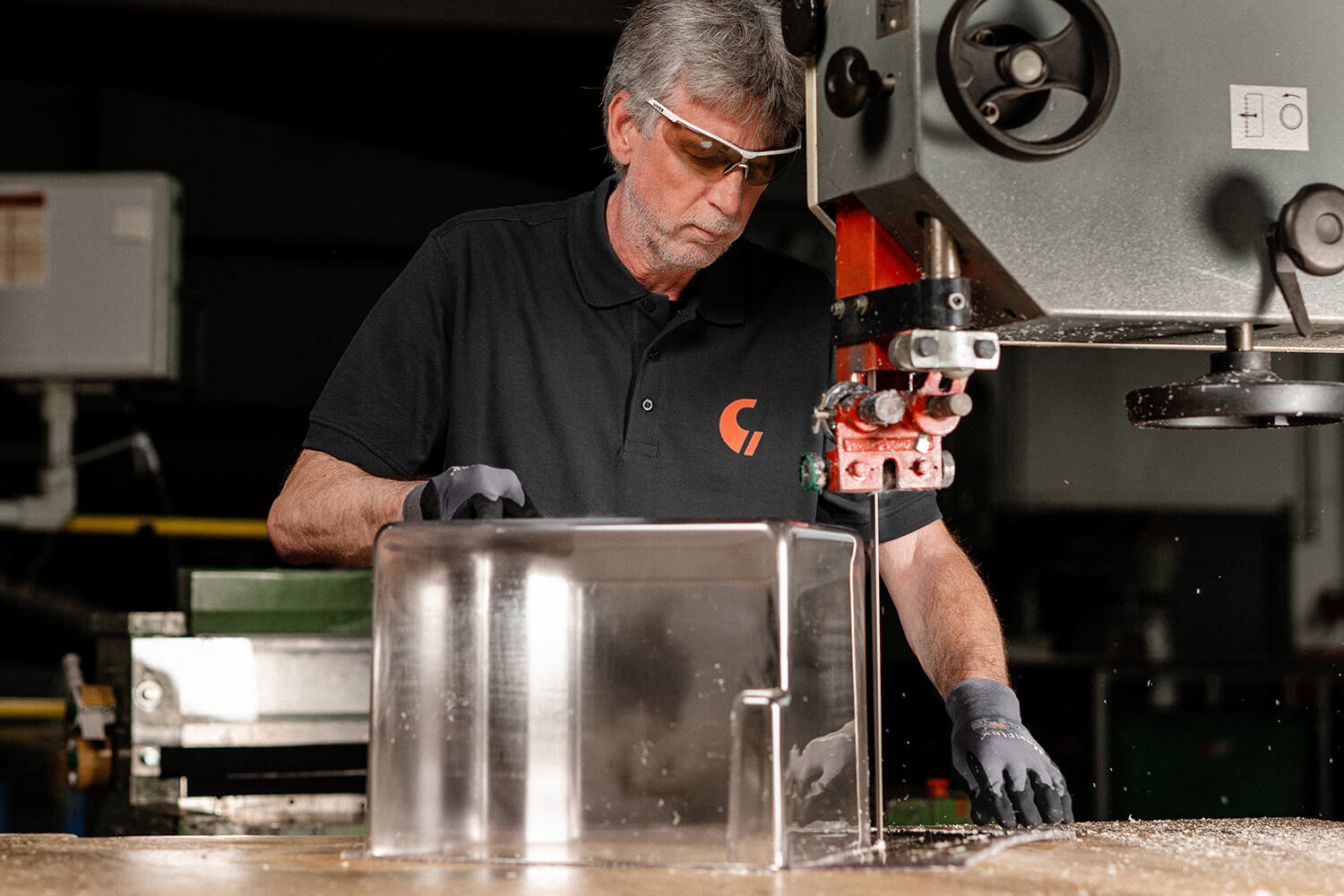 Ein Mitarbeiter mit Schutzbrille bearbeitet ein transparentes, frisch thermogeformtes Kunststoffteil.